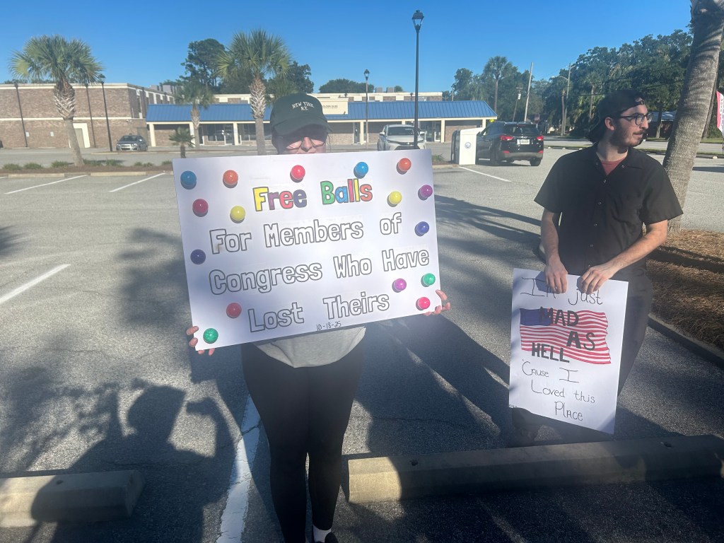 Protestors holding signs reading "Free balls for members of congress who have lost theirs" and "I'm just mad as hell 'cause I loved this place"