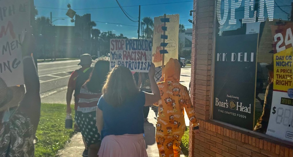 Protestor in Garfield costume, and another holding a sign reading "Stop pretending your racism is patriotism!"